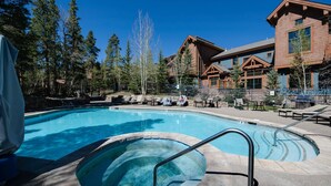 Een zwembadgedeelte met een jacuzzi, ligbedden en een houten lodge op de achtergrond.