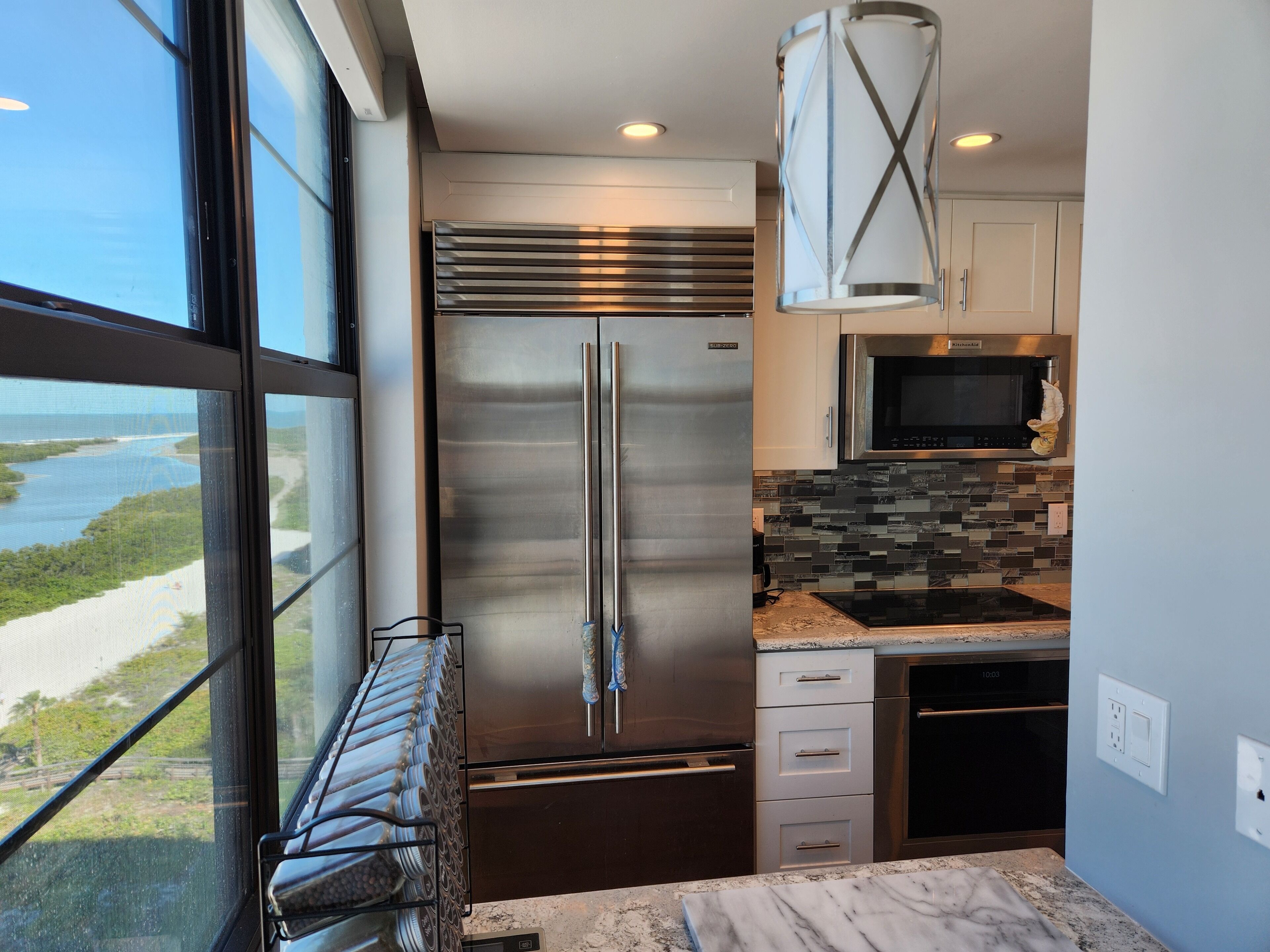 Una cocina moderna con un refrigerador de acero inoxidable, un microondas y un protector de salpicaduras de azulejos.