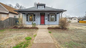 Ein eingeschossiges Haus mit roter Tür, einer kleinen Veranda und einer sichtbaren Garagentür.