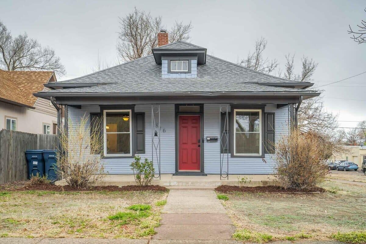 A single-story house with a red door, two windows on the front, and a small front yard with a pathway leading to the door.