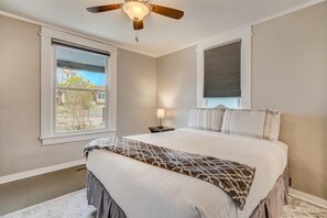 A bedroom with a bed, a ceiling fan, a window, and a nightstand with a lamp.