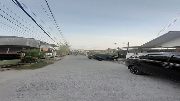 A residential street with houses on both sides, a black car parked on the right, and power lines overhead. - Hotel O Fermansio Homestay 2 (Medan)