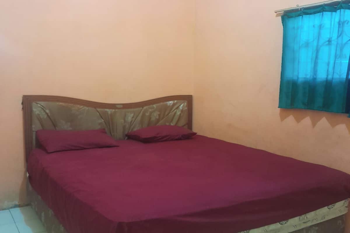 A single bed with a wooden frame and a floral-patterned mattress cover, a red bedspread, and two pillows.