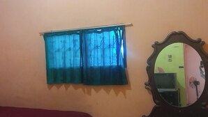 A bedroom with a bed, a dresser, a mirror, and a window with curtains. - Hotel O Fermansio Homestay 2 (Medan)