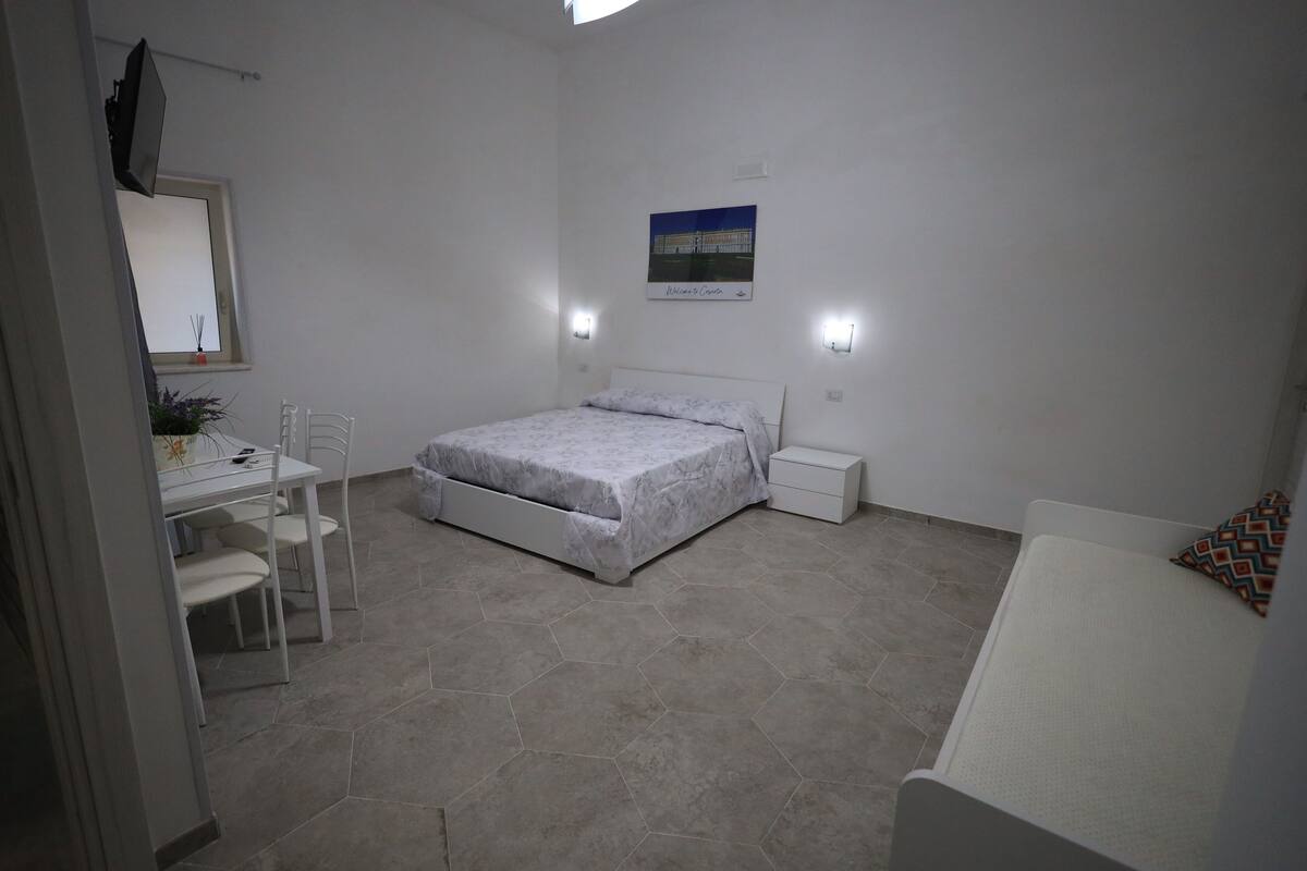 A bedroom with a bed, bedside tables, a desk with chairs, and a small window.