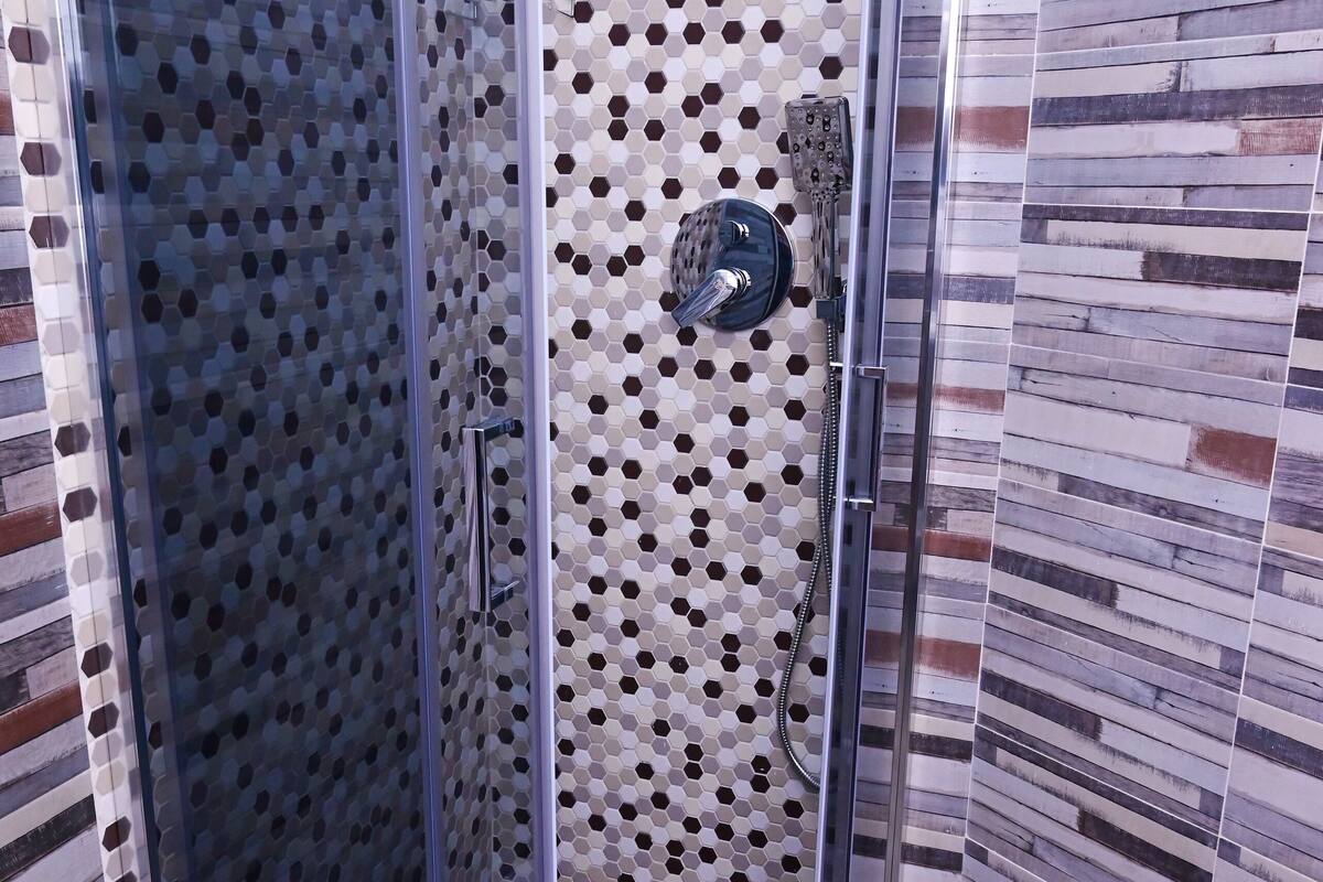A shower with a glass door, a rain showerhead, and a tiled wall with a hexagonal pattern.