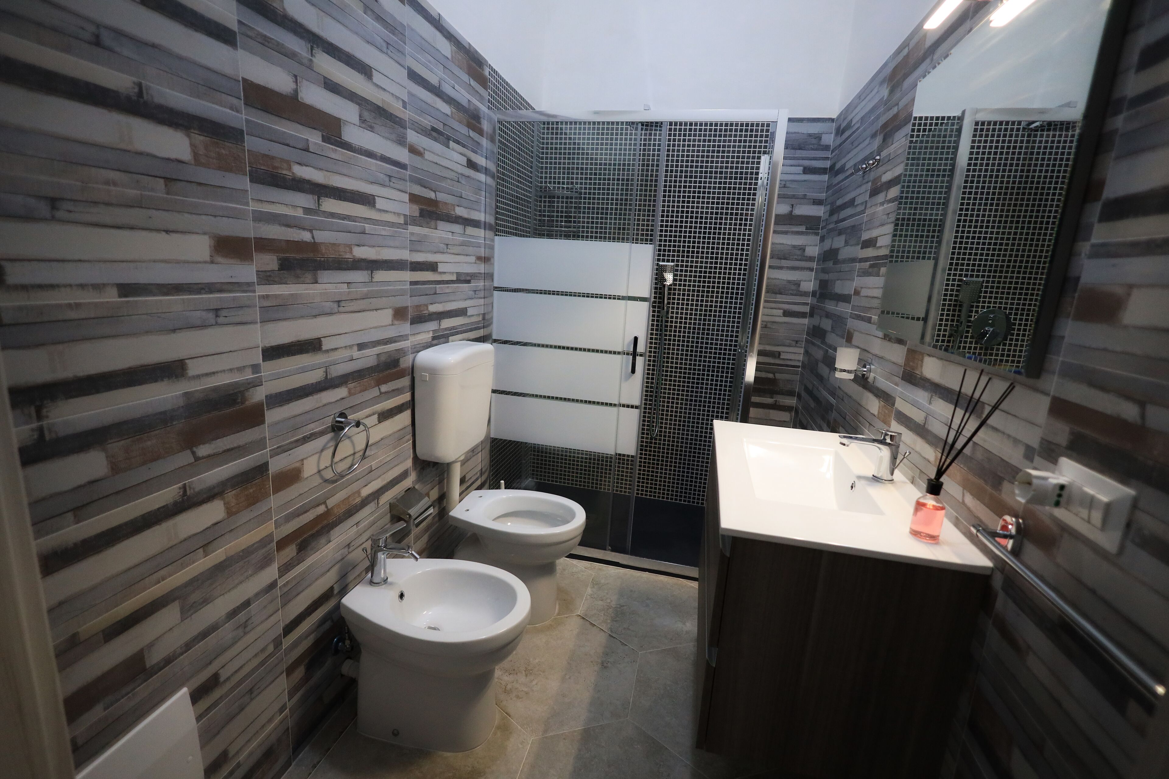 A modern bathroom with a shower, two bidets, a toilet, and a sink.