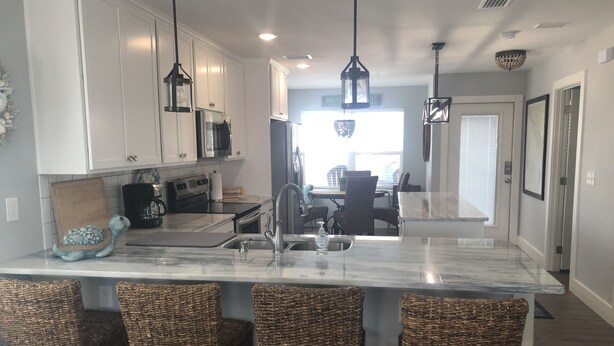 A modern kitchen with white cabinets, a marble island with bar stools, and pendant lighting.