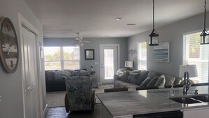 A modern kitchen with a built-in dishwasher, a dining area with a large island, and a living room with a sofa and a patterned armchair.