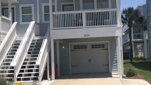 A two-story residential building with a garage, a balcony on the upper floor, and a staircase leading to the entrance.