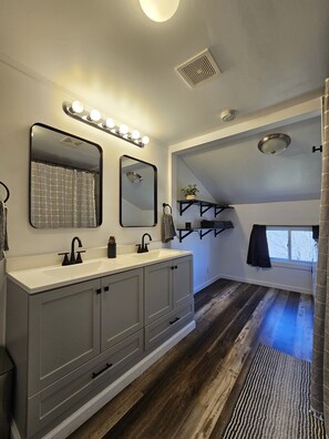 A modern bathroom with a large vanity, dual sinks, a mirror with lights, a shower, and a window with a view. - Charming Farmhouse in Oneonta, NY, 2 Mins away from Cooperstown All Star Village (Oneonta)