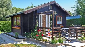 A wooden cabin with a porch, a small garden with flowers, and a windmill. - Ferienhaus Lassan bei Wolgast (Lassan bei Wolgast)