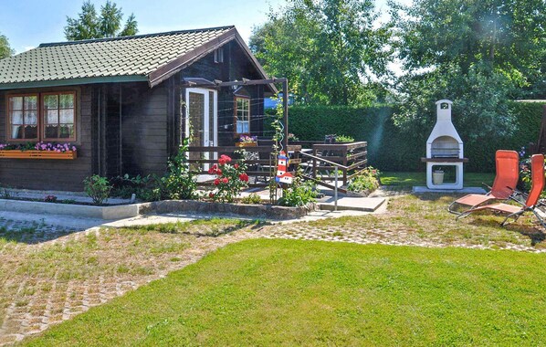 A wooden cabin with a porch, a small garden with flowers, and a barbecue area.