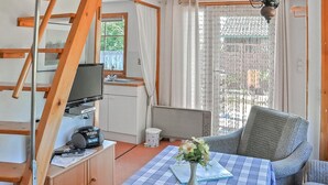 A compact kitchenette with a TV, a small fridge, and a coffee maker. There's a dining table with a checkered tablecloth and a vase with flowers. A chair is placed beside the table. - Ferienhaus Lassan bei Wolgast (Lassan bei Wolgast)