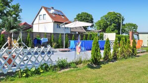 A two-story house with a red-tiled roof, solar panels, and a fenced backyard with a trampoline and a play structure. - Ferienhaus Lassan bei Wolgast (Lassan bei Wolgast)