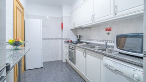 Una cocina moderna con armarios blancos, horno empotrado, microondas y lavavajillas.