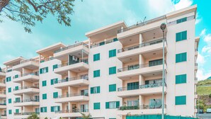 Un edificio residencial de varios pisos con balcones, un coche estacionado adelante y cielo despejado.
