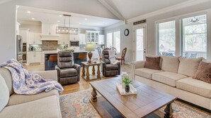 A spacious living room with a sofa, armchair, and coffee table. A kitchen with white cabinets and a dining area with a table and chairs are visible in the background. - Spacious Hot Springs Village Home < 1 Mi to Lake! (Hot Springs Village)