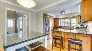 Une cuisine moderne dotée d’un îlot central avec un plan de travail en verre, de tabourets de bar en bois, d’appareils électroménagers en acier inoxydable et de grandes fenêtres.