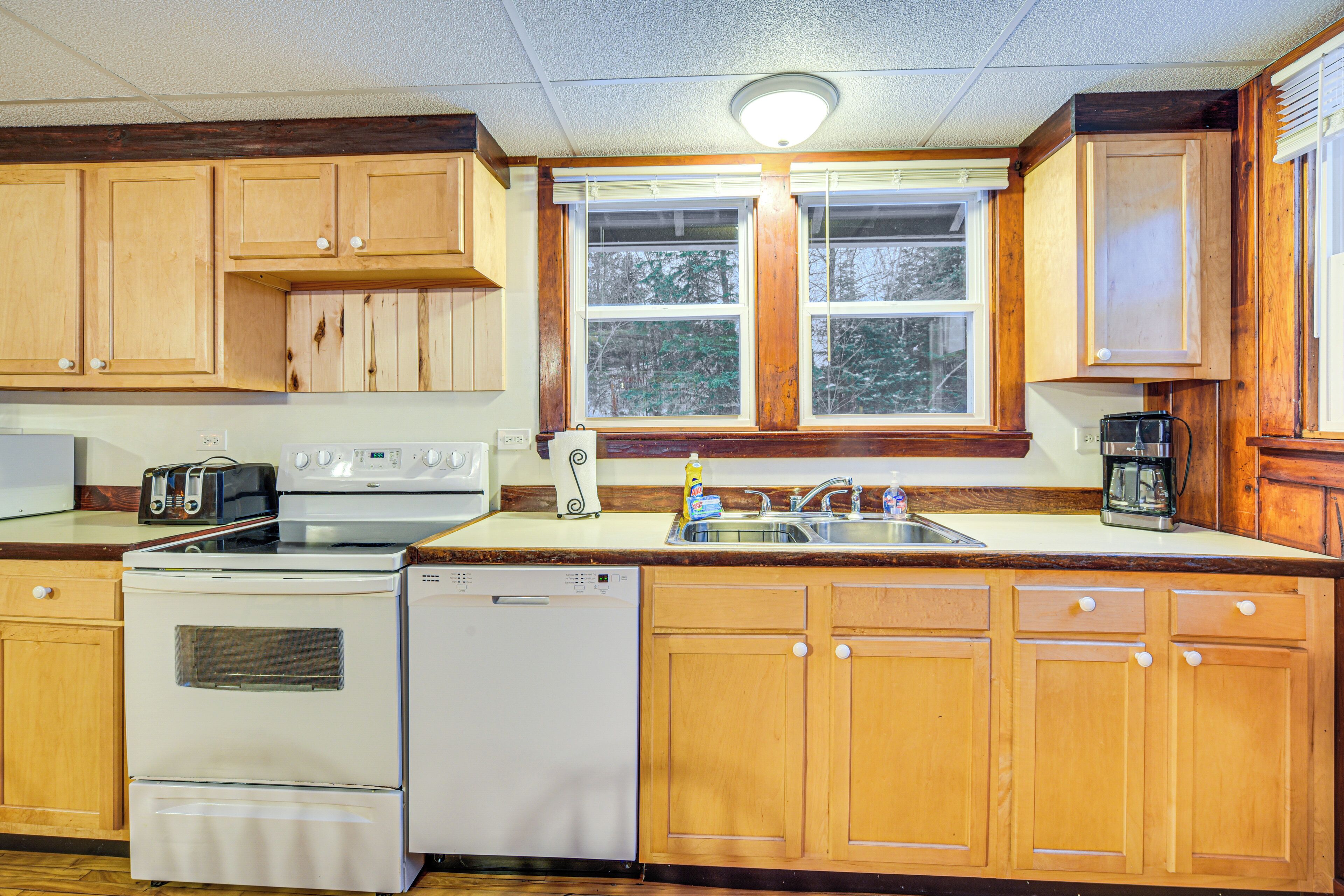 Una cocina con armarios de madera, estufa, lavavajillas y ventana con vista a árboles.