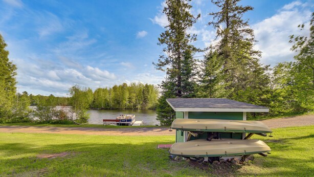 A lakeside cabin with a small dock, surrounded by lush greenery and a clear sky. - Hayward Retreat on the Chippewa Flowage w/ Dock! (Hayward)
