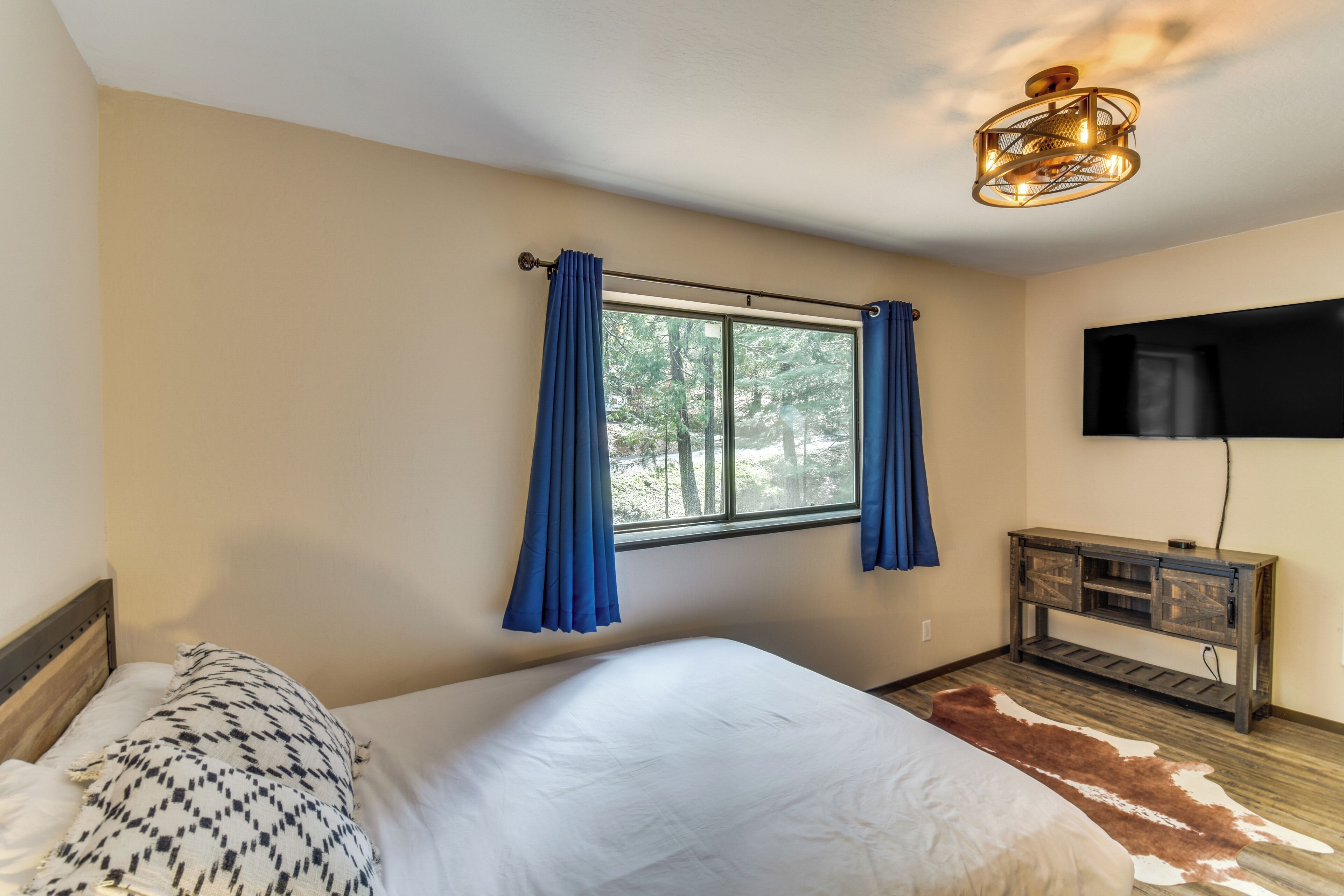 A bedroom with a bed, a window with curtains, a television, and a wooden cabinet.