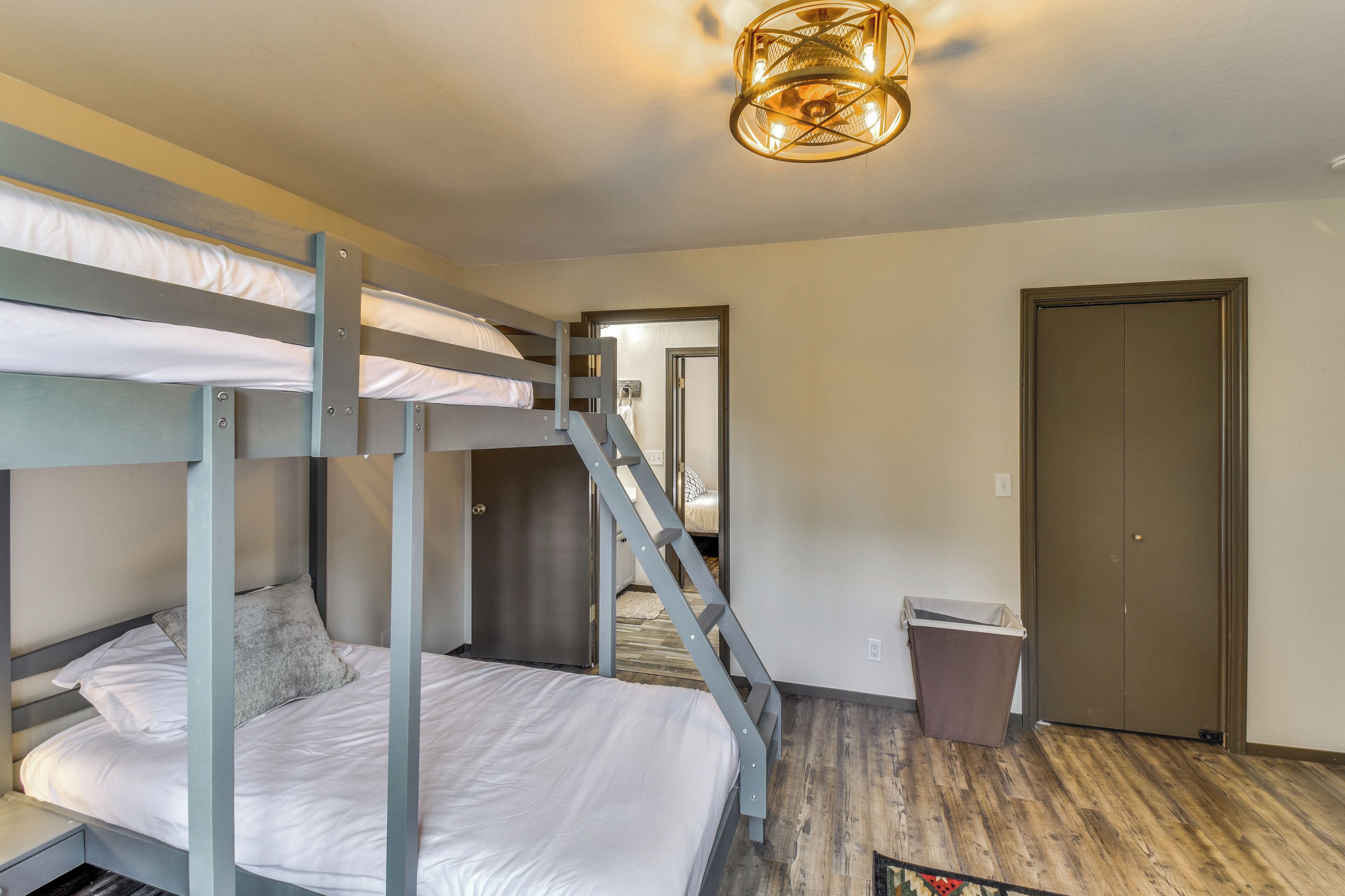 A bunk bed room with a staircase leading to a door, a trash bin, and a ceiling light fixture.