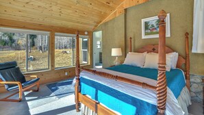 Ein Bett mit Baldachin, ausgestattet mit einer blauen Bettdecke, unter einer Holzbalkendecke mit Blick ins Freie durch große Fenster.