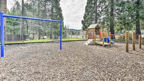 A playground with a blue swing set, a wooden playhouse, and a slide. - Game Room + Pool Access: Spacious Cabin in Arnold (Arnold)