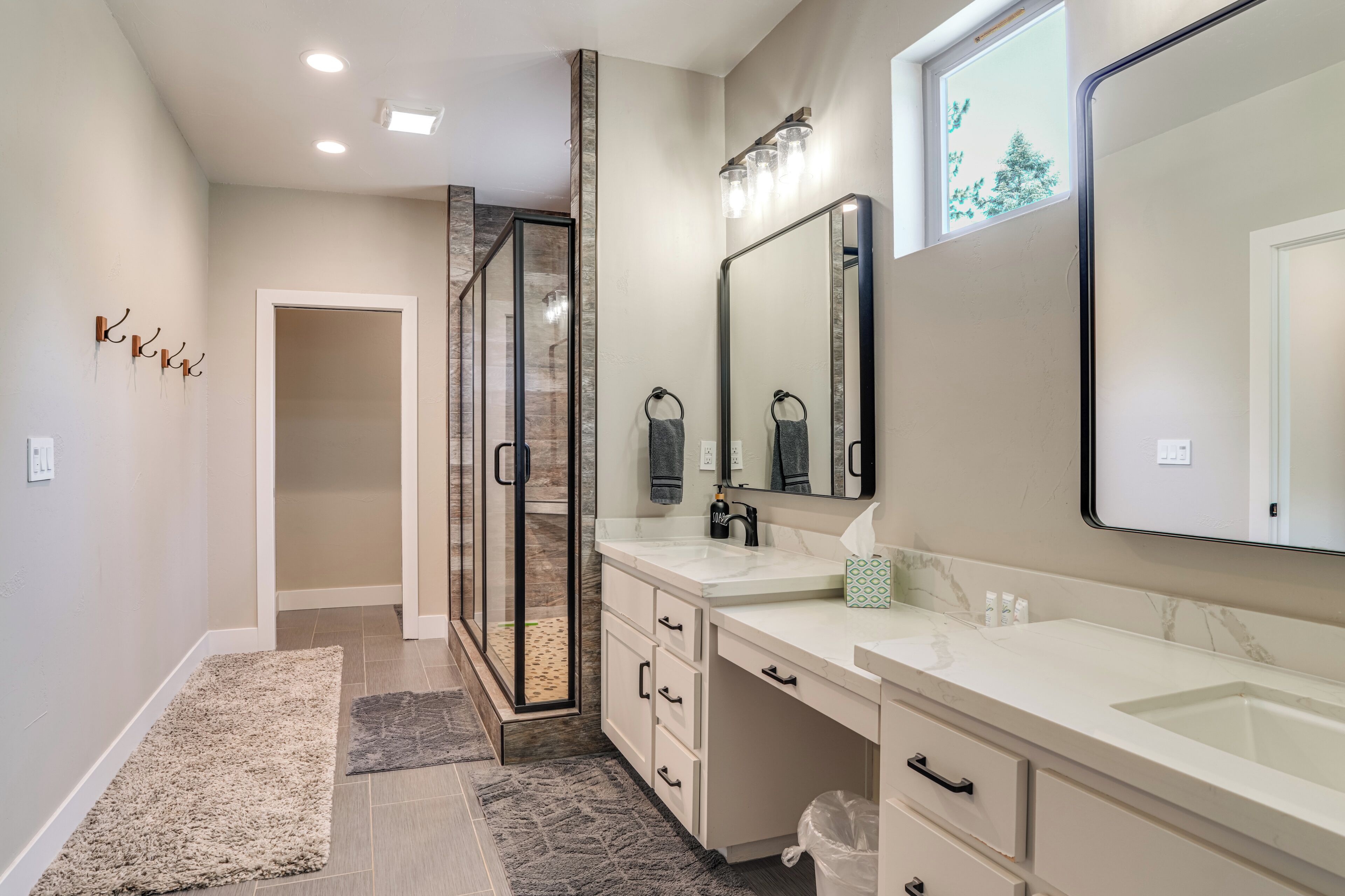 Un baño moderno con un espejo grande, dos lavamanos, ducha a ras de suelo y una puerta que da a otra habitación.