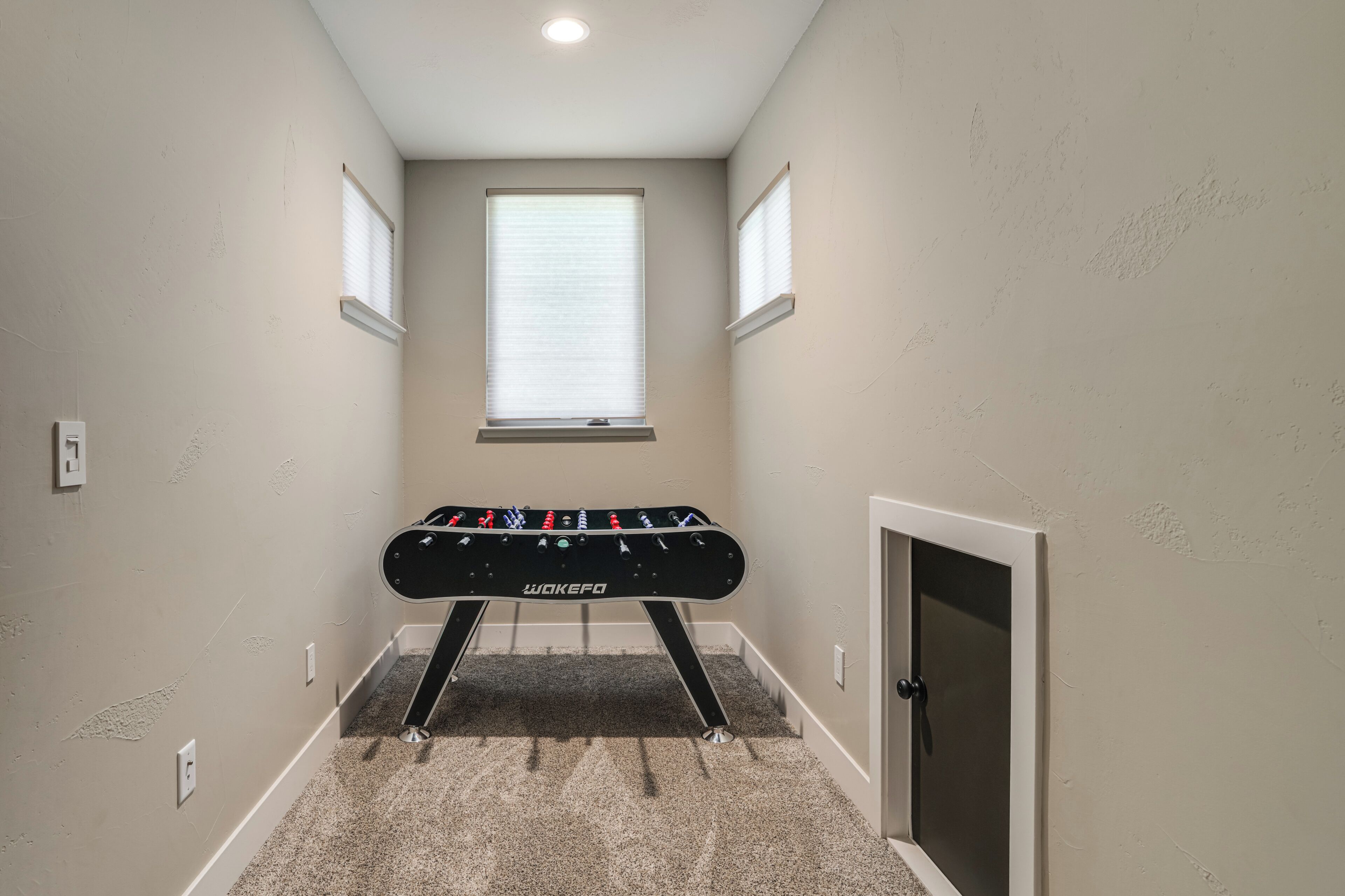 A narrow hallway with a foosball table, a window, and a door.