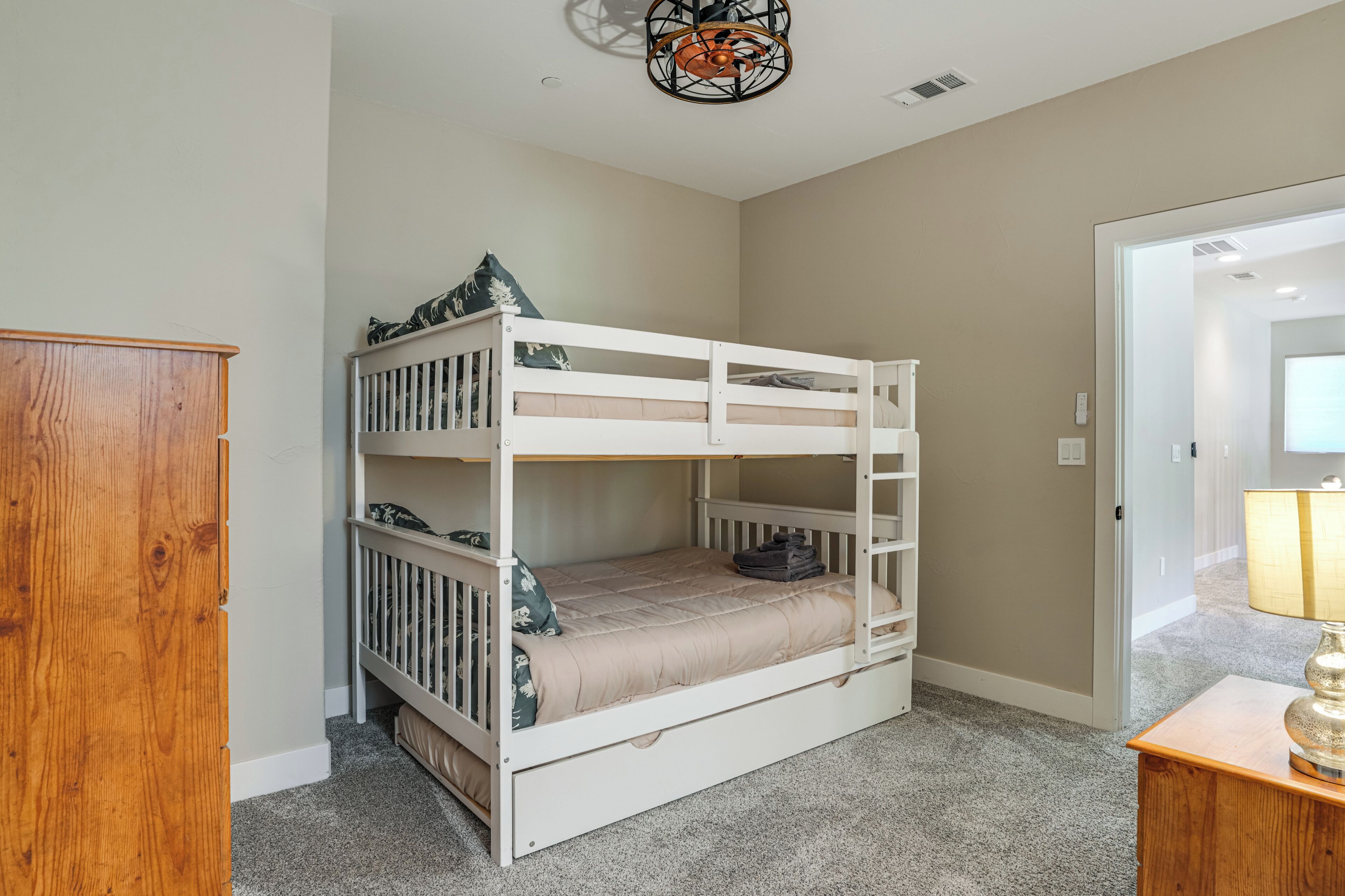 A bunk bed in a room with a wooden wardrobe, carpeted floor, and a door leading to another room.