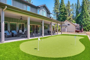 Une maison dotée d’un patio couvert, d’une pelouse avec un green d’entraînement et d’un garage.