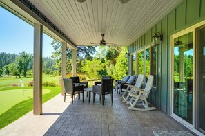 Une véranda aménagée avec des meubles d’extérieur, de grandes fenêtres et une vue sur un terrain de golf.