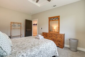 A bedroom with a bed, dresser, mirror, and a hallway leading to another room.