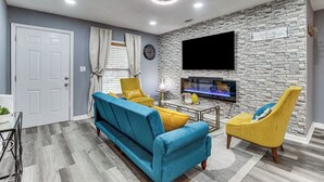 Ein Wohnzimmer mit einer Couch, Sesseln, einem Fernseher und einer Steinwand.