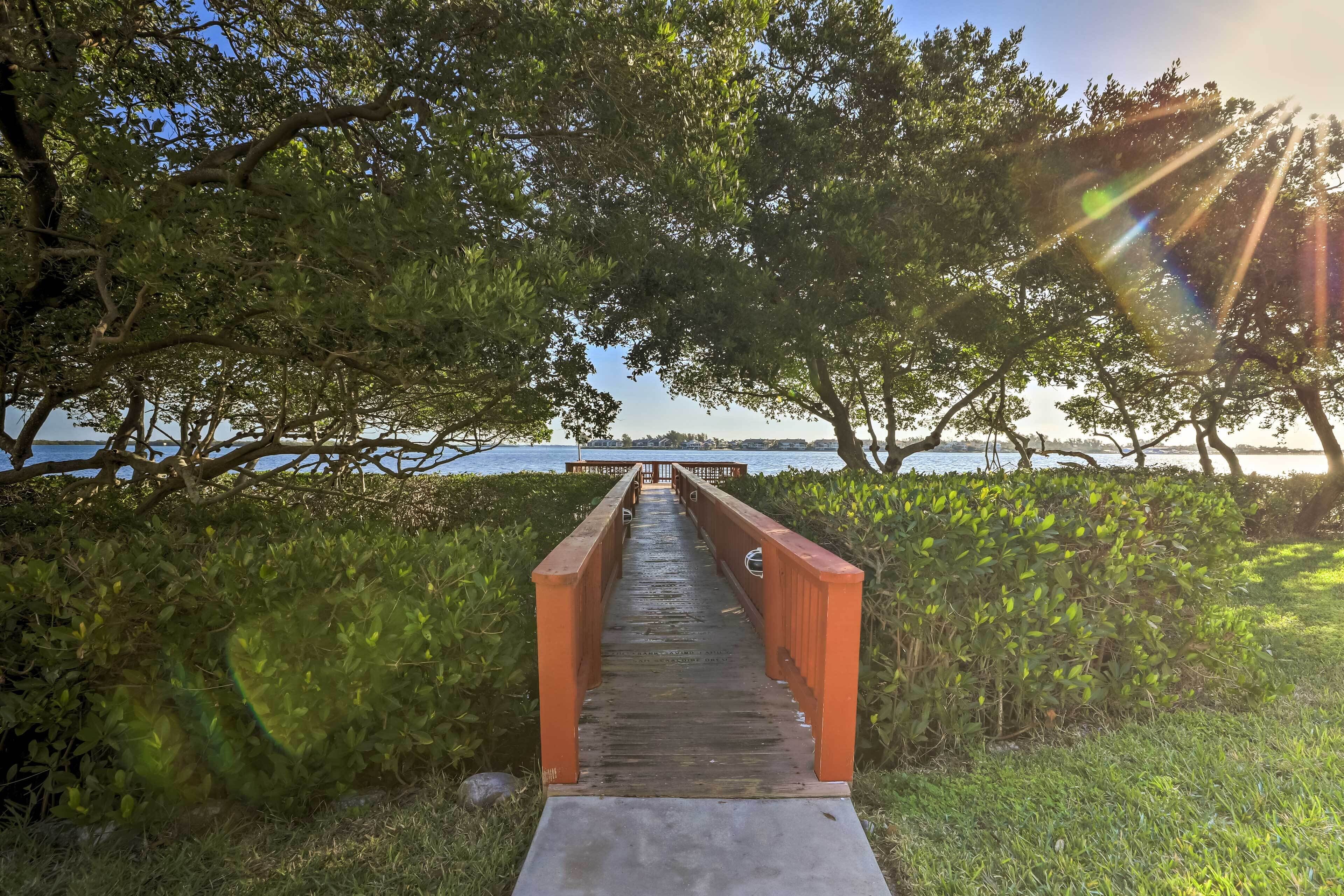 A wooden pathway leading to a bridge over water, surrounded by greenery.