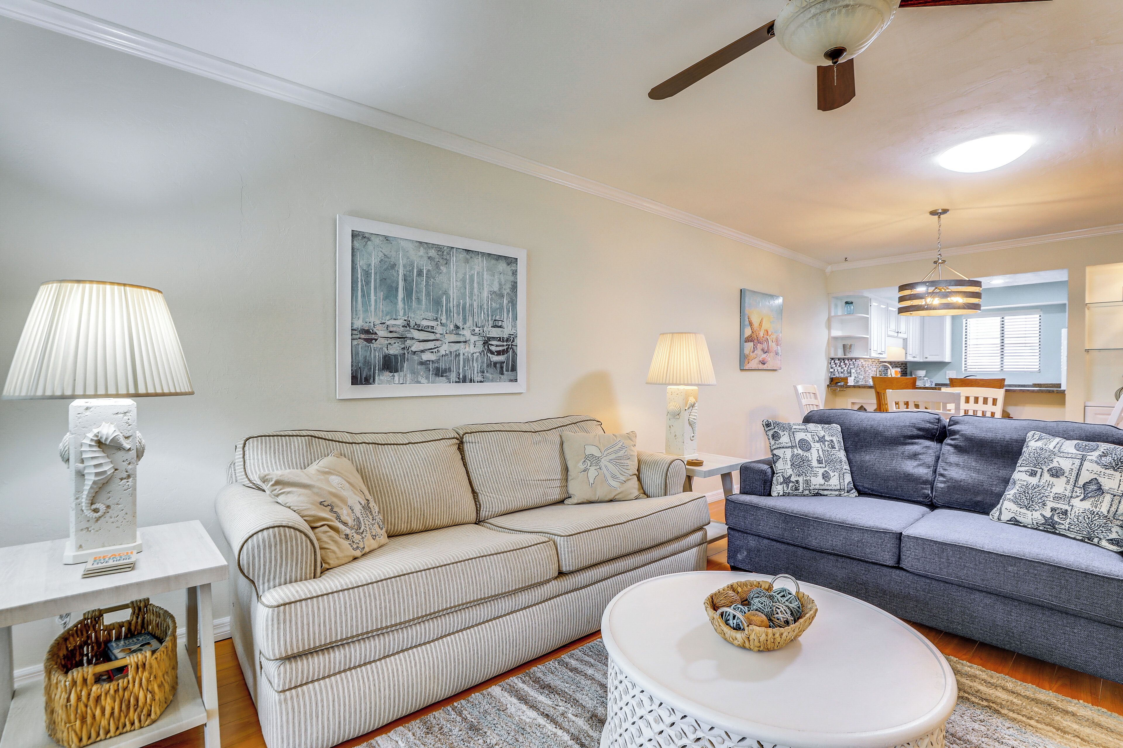 A living room with a striped sofa, a grey sofa, a white coffee table, and a ceiling fan.