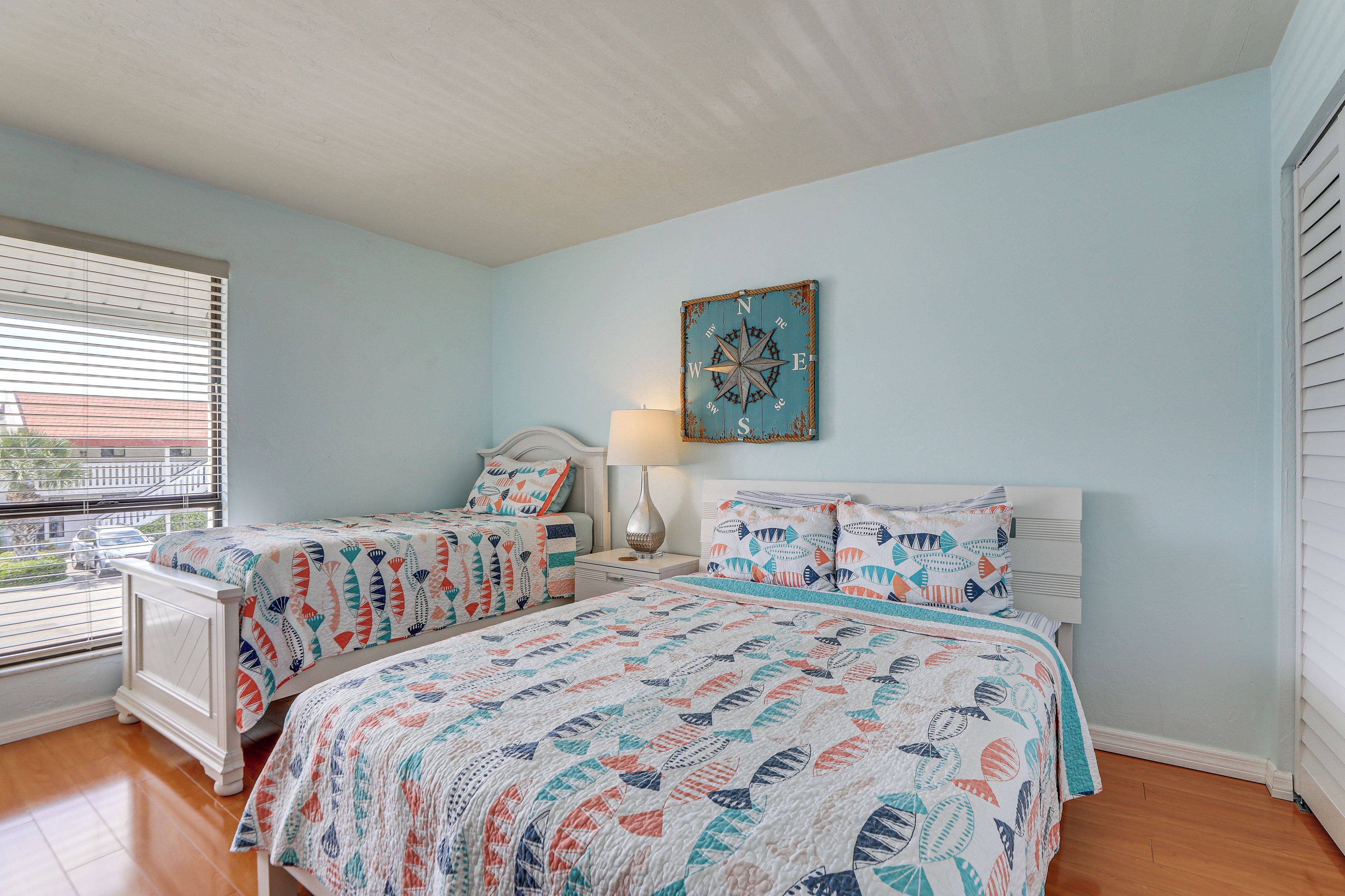 Une chambre avec deux lits, une décoration murale représentant une boussole, une fenêtre avec des stores et une table de chevet avec une lampe.