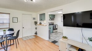 A modern kitchen with a flat-screen TV, wooden cabinets, and a dining area with a table and chairs. - Jefferson City Bungalow: Hot Tub & Patio! (Jefferson City)