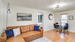 A living room with a brown leather sofa, a dining table with four chairs, a ceiling fan, and a painting of a landscape on the wall. - Jefferson City Bungalow: Hot Tub & Patio! (Jefferson City)