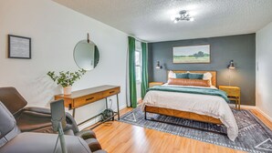 A bedroom with a bed, bedside tables, a desk, a chair, a mirror, and a potted plant. - Jefferson City Bungalow: Hot Tub & Patio! (Jefferson City)