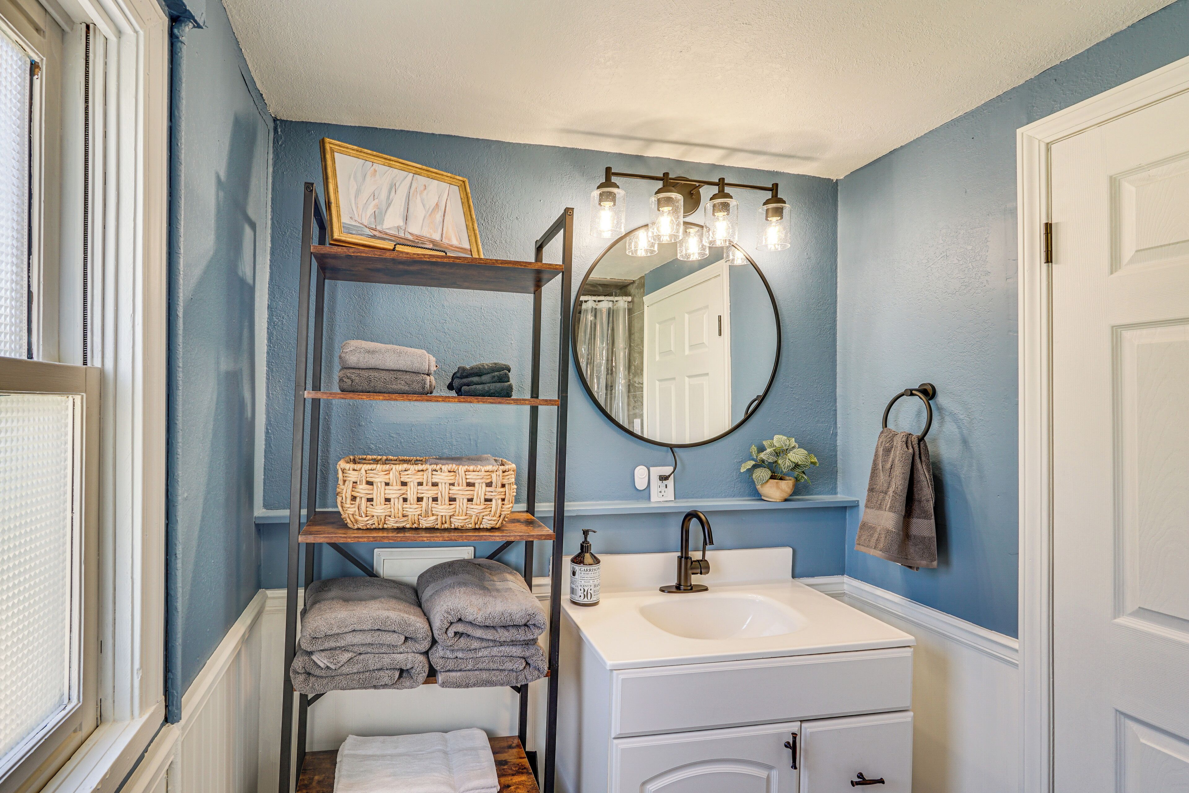 A bathroom with a white sink, a mirror, and shelves holding towels and a basket.