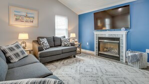 A living room with a gray sofa, a fireplace, a flat-screen TV, and a framed picture on the wall. - Angola Vacation Rental, Walk to Lake Erie Beach! (Angola)