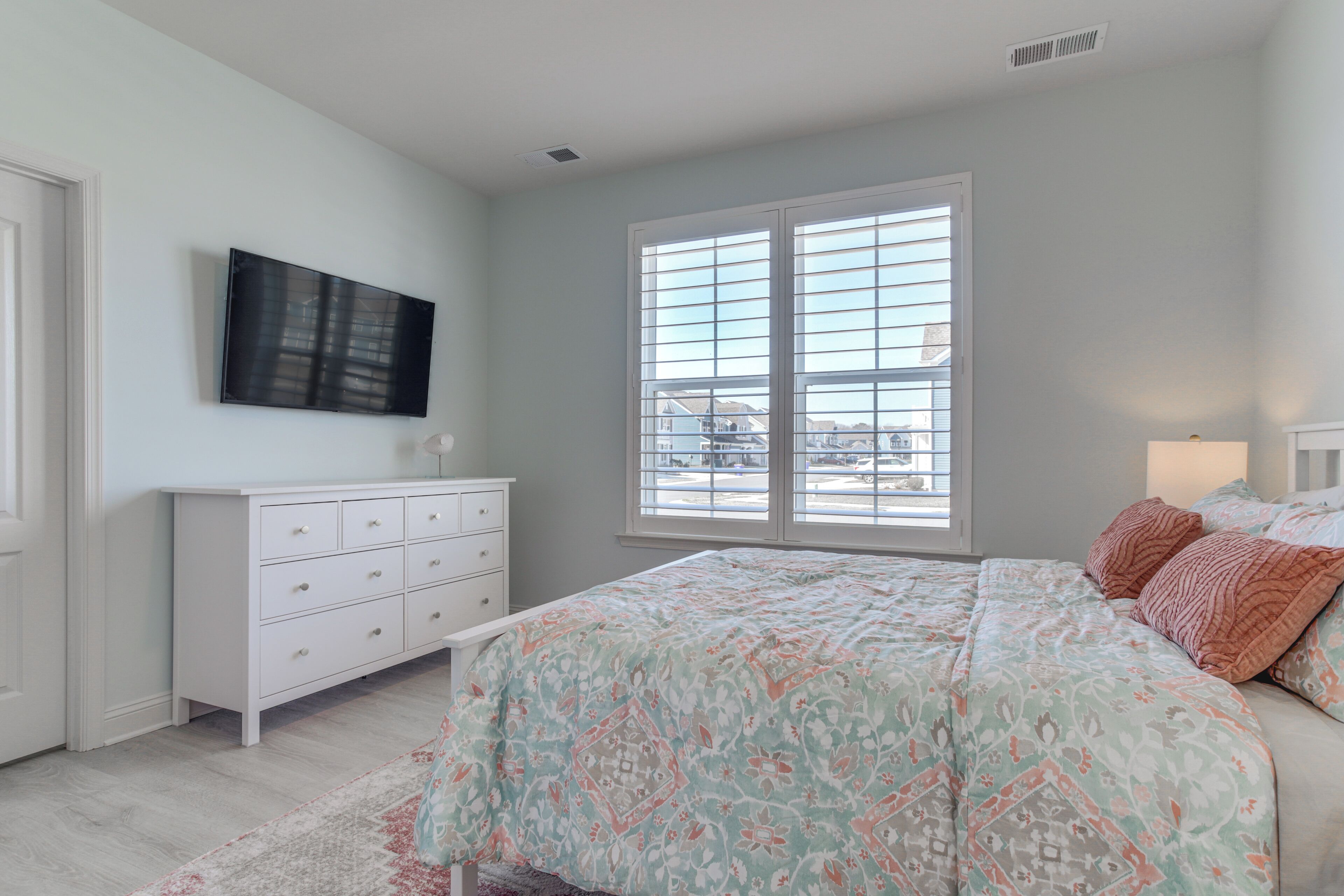 A bedroom with a bed, dresser, TV, and large window.
