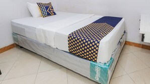 A bed with a white mattress, a blue and yellow patterned blanket, and a single pillow with a similar pattern. - Hotel O Budi Residence 2 (Bekasi)