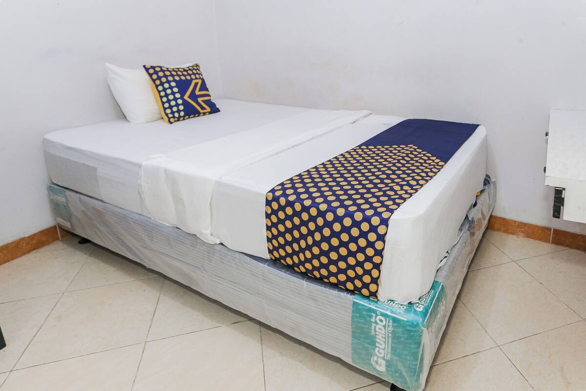 Een bed met een witte matras, een deken met een blauw-geel patroon, en een kussen met een vergelijkbaar dessin.