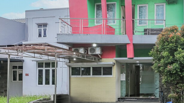 A multi-story building with a green and red facade, a balcony, and a bicycle parked outside. - Hotel O Budi Residence 2 (Bekasi)