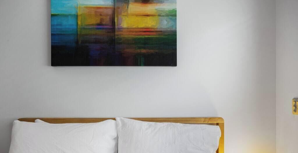 A room with a bed, a white pillow, and a colorful abstract painting on the wall.