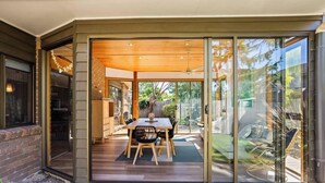 A modern dining area with a glass door leading to a patio, a wooden ceiling, and a brick wall. - Beach Access Home with Private Outdoor Retreat (Cowes)